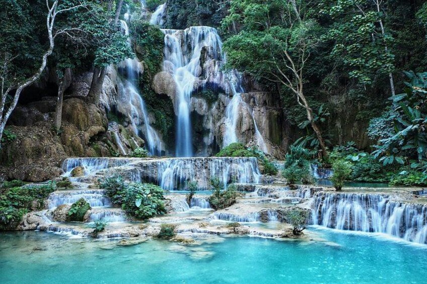 A waterfall cascading over rocky formations into a turquoise pool surrounded by lush greenery. 1