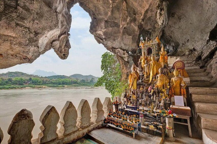 A rock formation with a cave opening, a river, and a collection of golden statues. 5