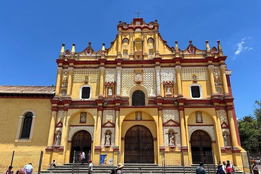 Una iglesia grande y ornamentada con fachada amarilla y detalles en rojo, que presenta múltiples arcos y estatuas. 2
