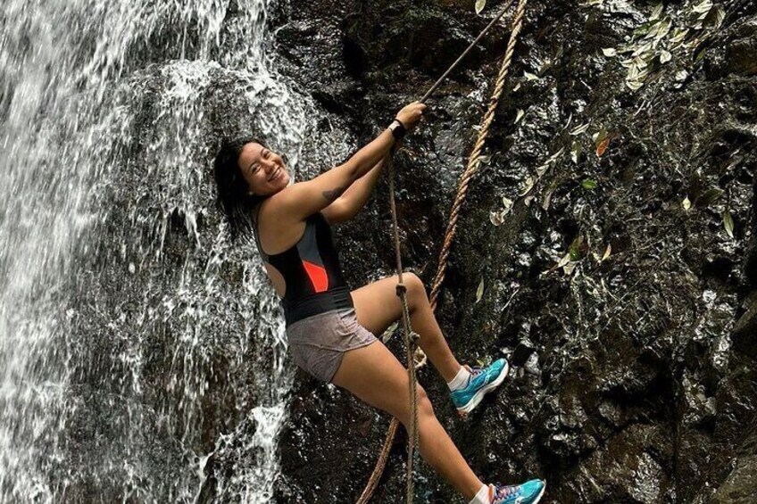 A person rappelling down a rocky cliff with a waterfall in the background. 2