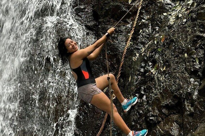 A person rappelling down a rocky cliff with a waterfall in the background. 4