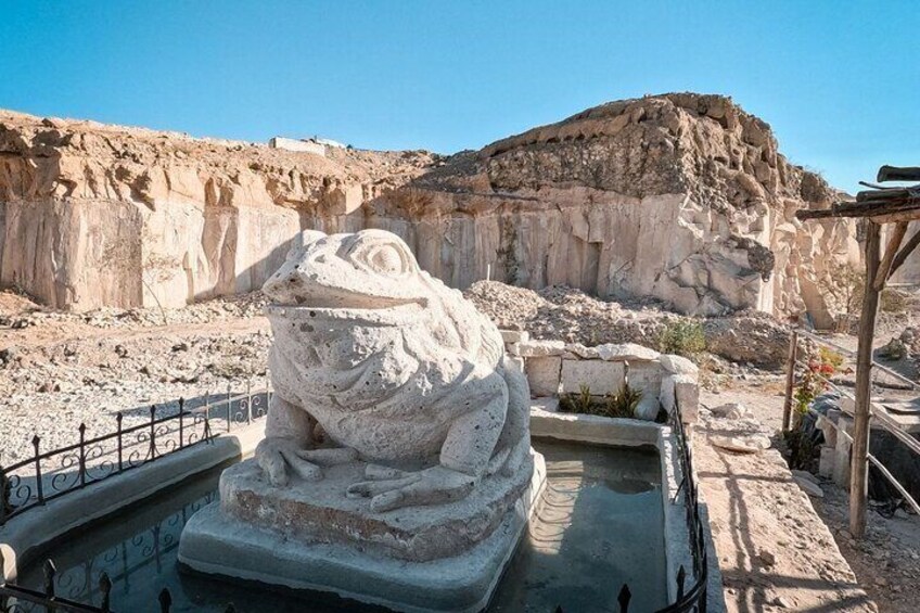 A large stone frog statue in a desert setting with rocky cliffs in the background. 1