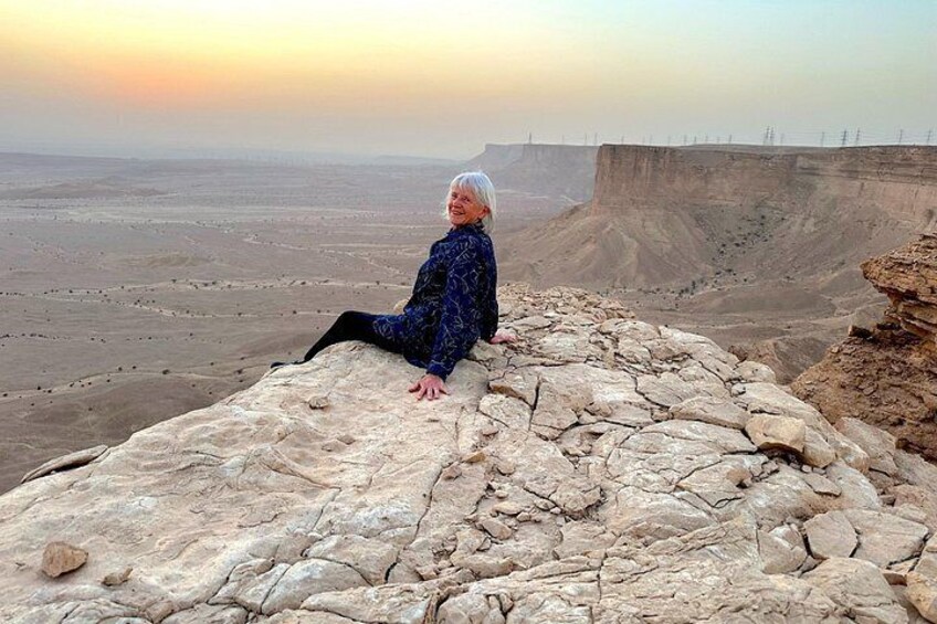 Una persona sentada sobre un afloramiento rocoso con vistas a un extenso paisaje y un horizonte lejano. 1