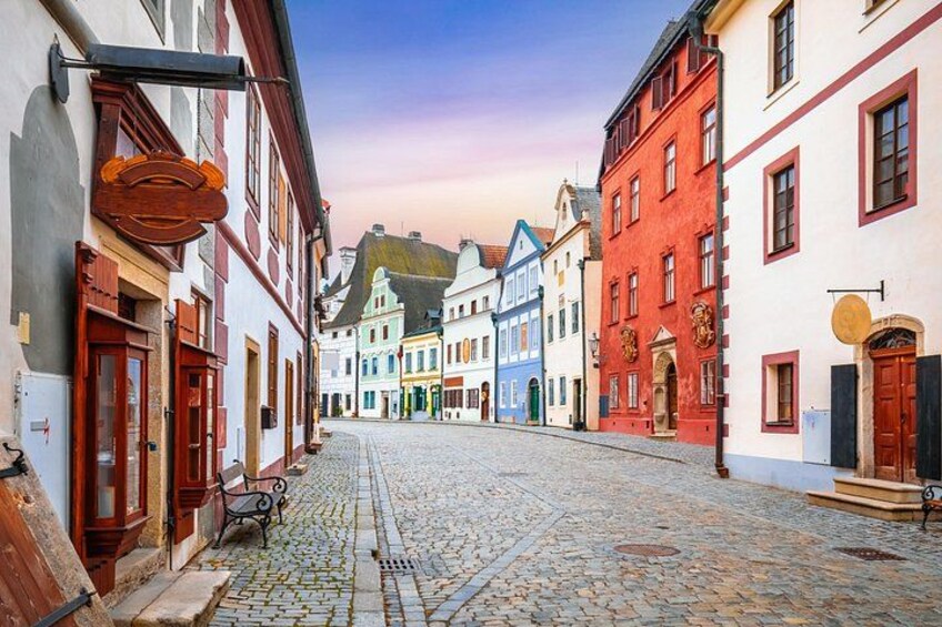 A cobblestone street lined with colorful buildings, a bench, and a street lamp. 3