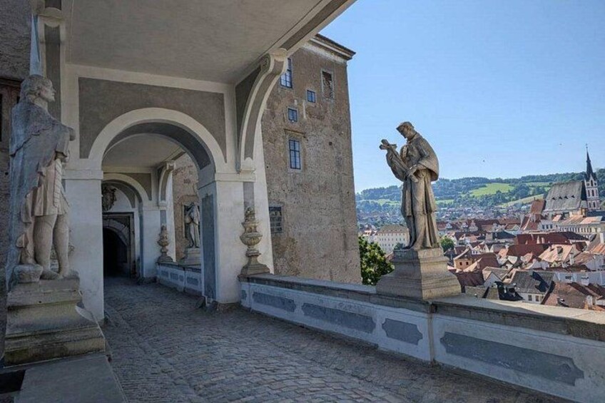 A cobblestone pathway leading to a building with statues and a view of a town. 4