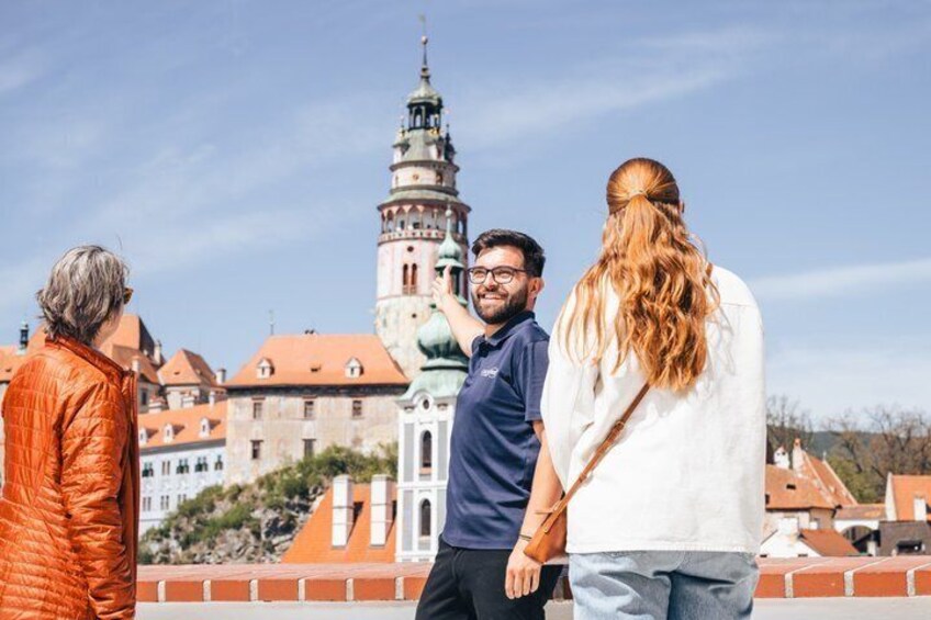 A group of people standing on a rooftop overlooking a historic building with a tower. 1