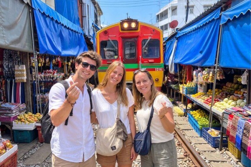 A train on tracks with people standing in front of a market. 4