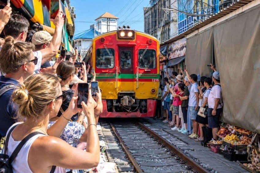 A train on tracks with people taking photos and a market stall on the right. 1