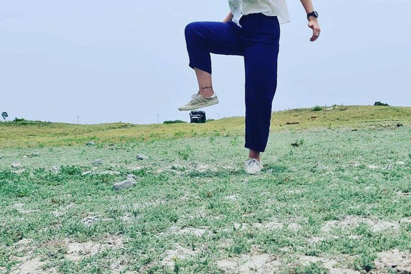 A person in motion, wearing white shirt and blue pants, on a grassy field with a clear sky. 2