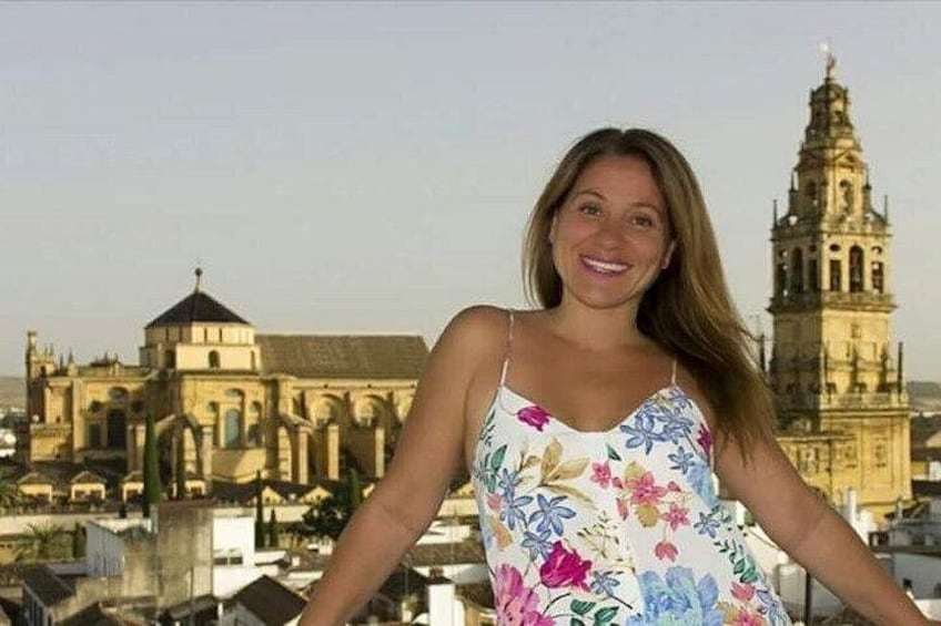 A person standing with arms outstretched in front of a historic building with a bell tower. 3