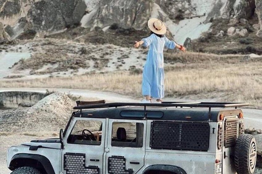 A person standing on a vehicle in a rocky outdoor setting. 1