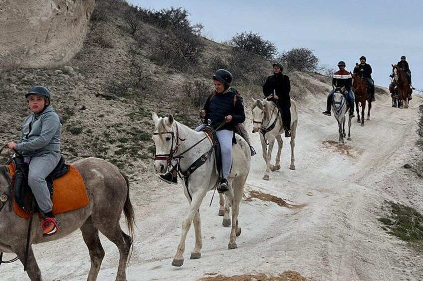 A group of people riding horses on a dirt road surrounded by rocky terrain. 2