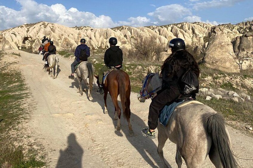 A group of people riding horses on a dirt path through a rocky landscape. 3