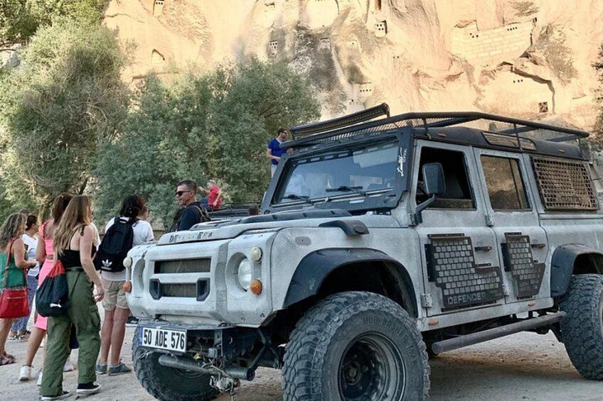 A rugged off-road vehicle parked in a rocky outdoor setting with people standing nearby. 5