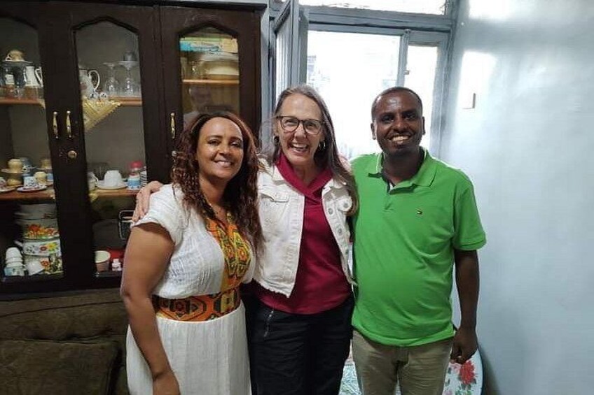 Three people standing indoors with a wooden cabinet and a window in the background. 2