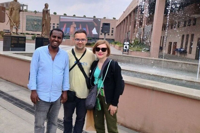 Three people standing in front of a building with a fountain. 1