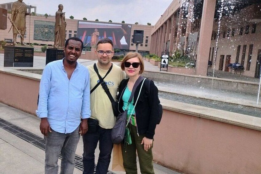 Tres personas frente a un edificio con una fuente. 1