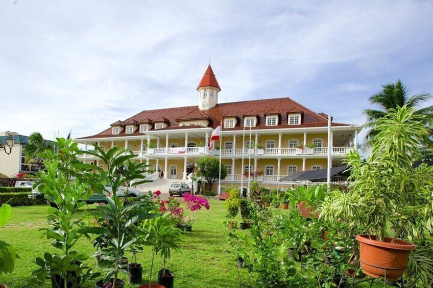 A large building with a red roof and a tower, surrounded by a well-maintained garden with various plants and flowers. 3