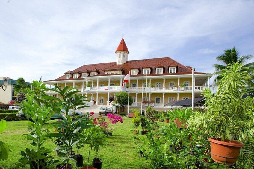 A large building with a red roof and a tower, surrounded by a well-maintained garden with various plants and flowers. 3