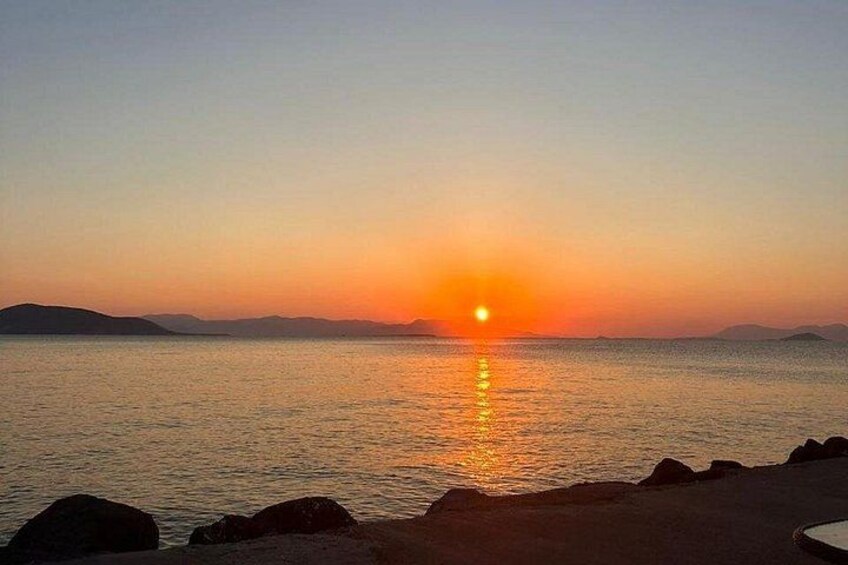 A sunset over a calm sea with a rocky shoreline. 1