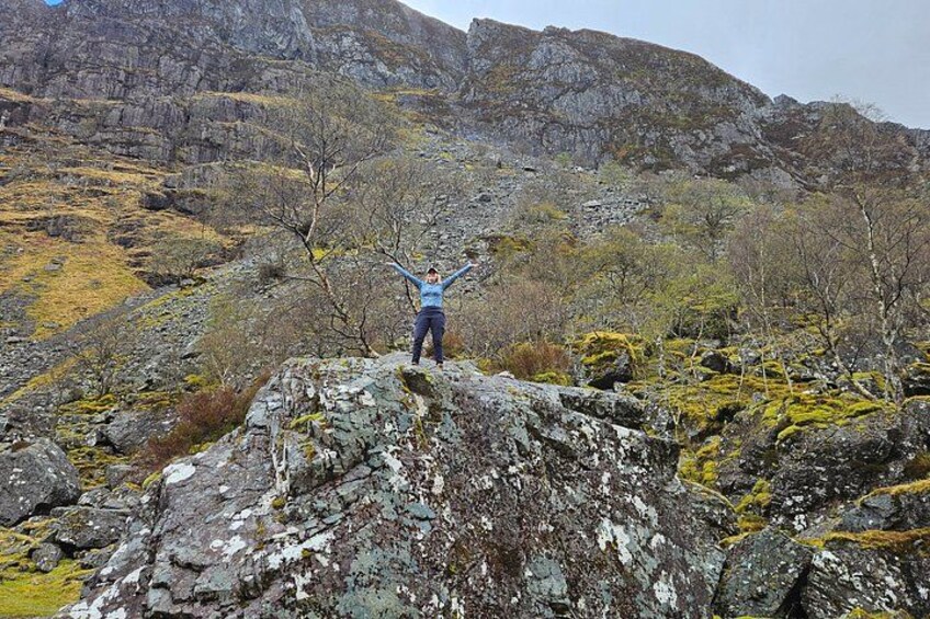 Une personne se tient debout sur un promontoire rocheux, les bras levés, et est entourée d’un paysage montagneux. 3