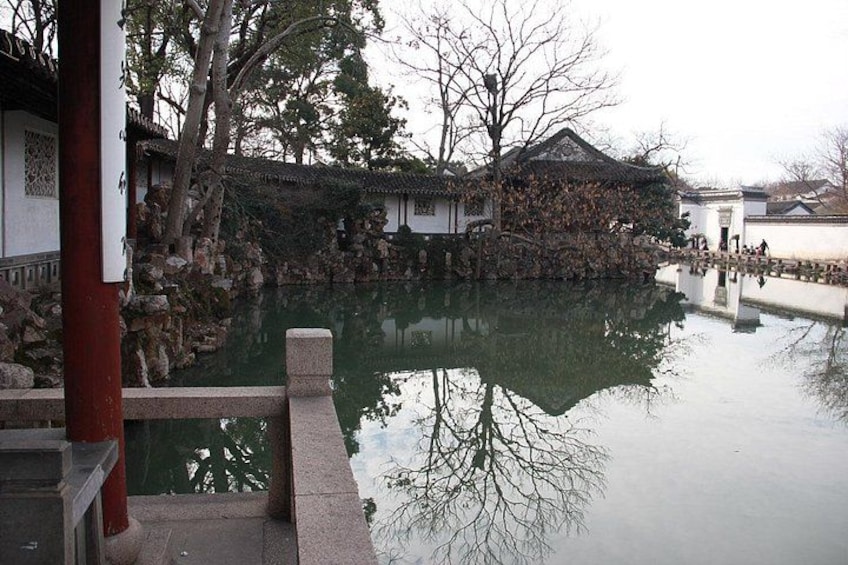 A traditional Chinese courtyard with a pond, stone bridge, and buildings with tiled roofs. 5