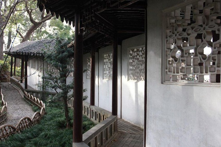 A traditional Chinese garden with a stone bridge, wooden walkway, and intricate wall carvings. 3