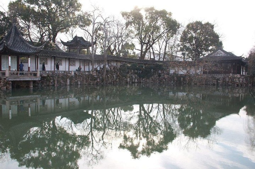A traditional Chinese pavilion by a calm pond with reflections, surrounded by trees and stone walls. 2