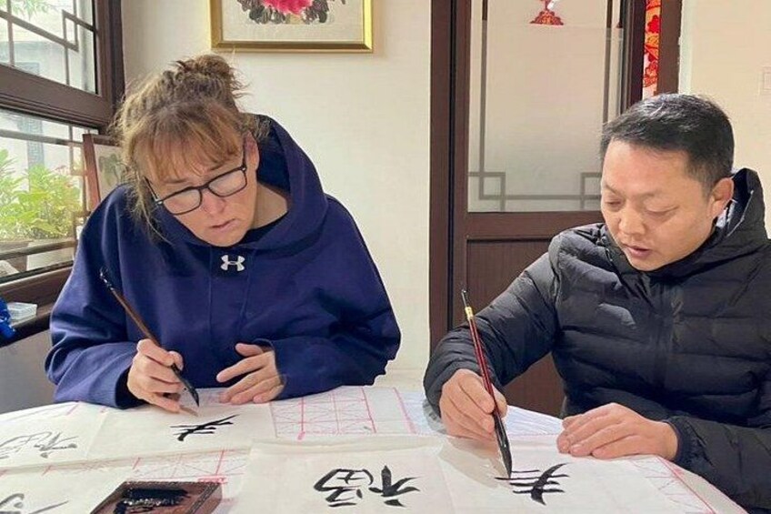 Dos personas sentadas a una mesa con papel de caligrafía, una escribiendo y la otra observando. 4