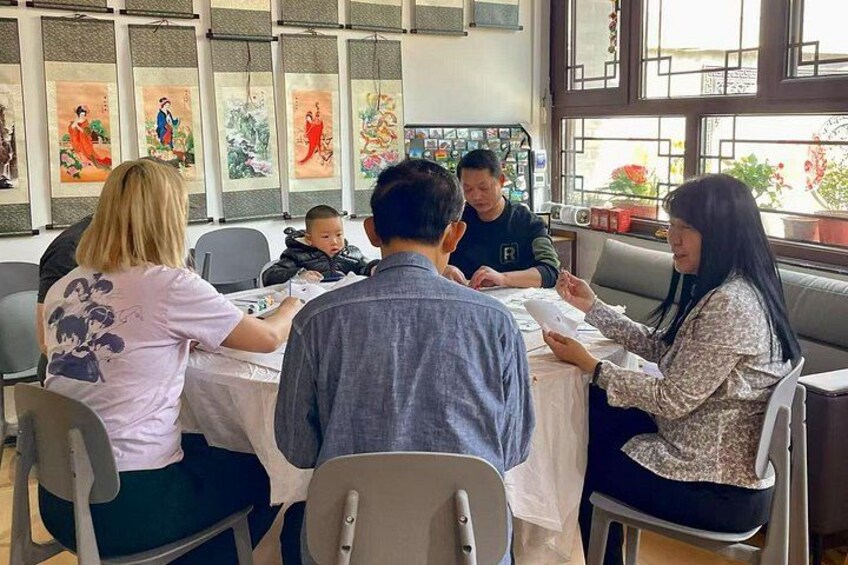 Un grupo de personas sentadas alrededor de una mesa en una habitación con pinturas tradicionales chinas en las paredes. 1