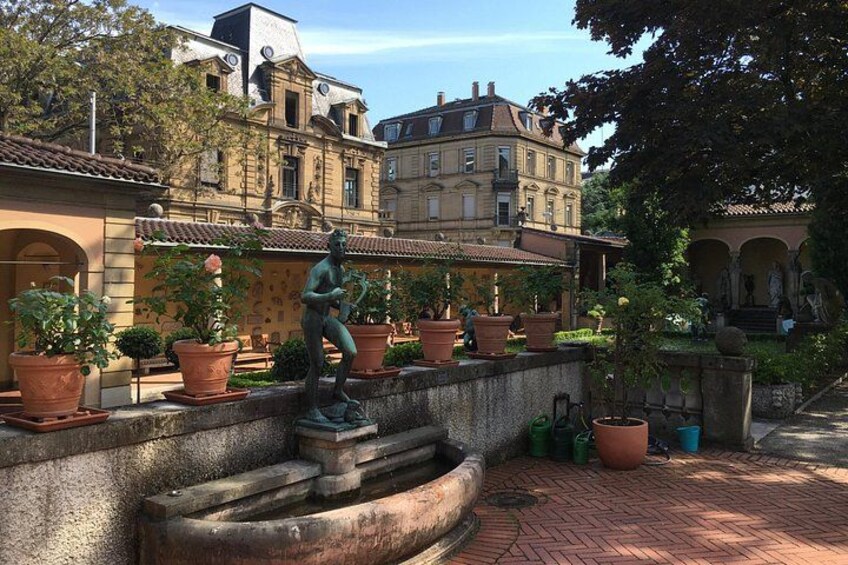 A courtyard with a fountain, potted plants, and classical architecture. 2