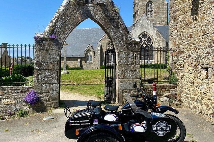 A stone archway, a church, and a motorcycle parked in front. 4