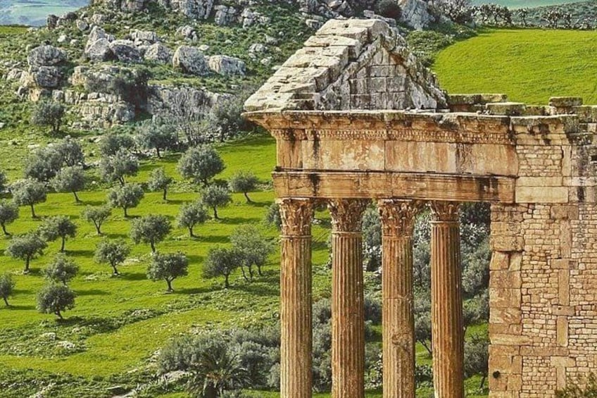 Ancient columns, a stone structure, and olive trees in a hilly landscape. 2