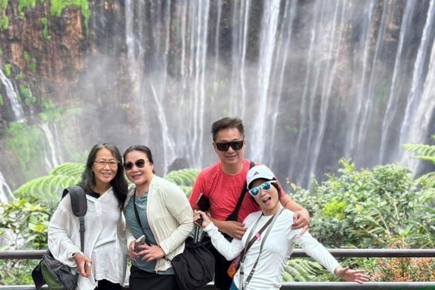 Eine Gruppe von Personen posiert vor einem Wasserfall, im Hintergrund üppiges Grün. 5