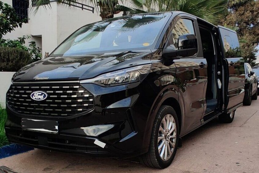 A black Ford van parked on a paved surface with a building and palm trees in the background. 2