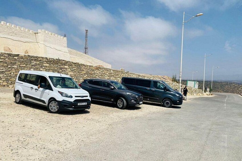 A white and a black car parked on a road with a stone wall and a clear sky in the background. 5