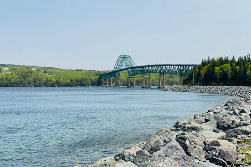A river with a green bridge, rocky shore, and forested hills. 2