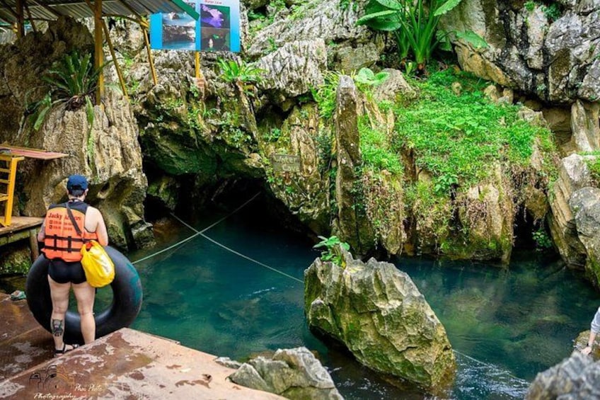 A person in a life jacket and helmet standing on a platform, holding a rope, with a rocky cave and water below. 2