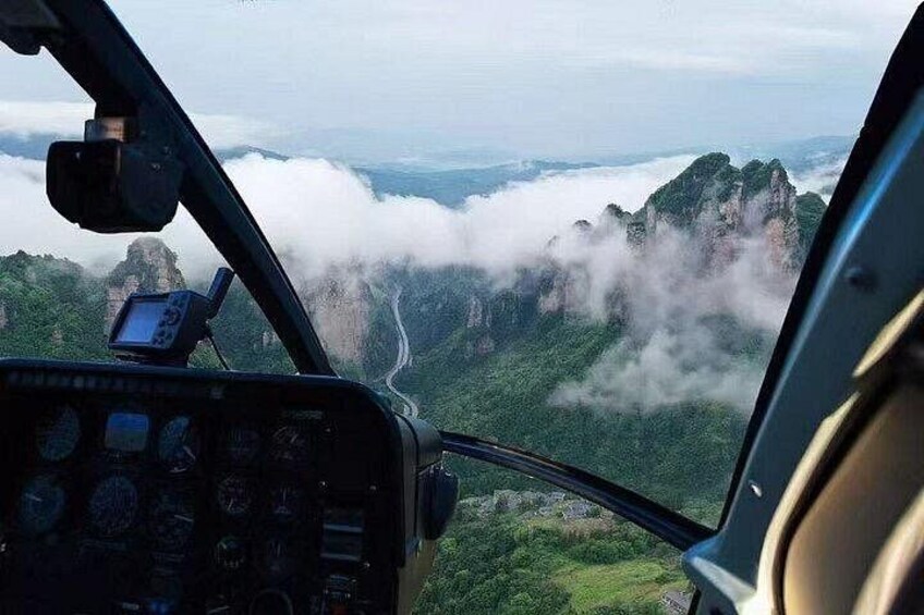 A helicopter cockpit with a view of a mountainous landscape and clouds below. 3