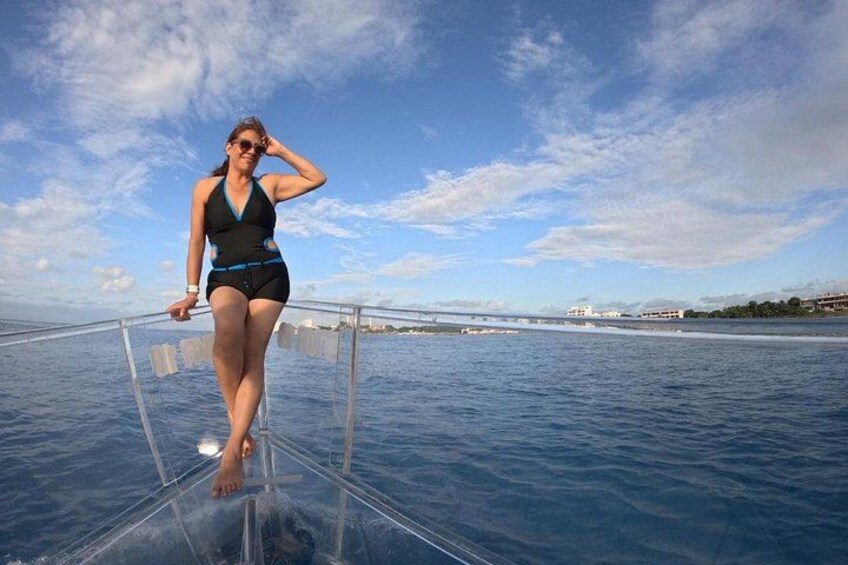 A person standing on a transparent platform over water, with a clear sky and distant buildings. 4