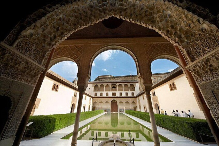 An ornate archway with intricate designs, a courtyard with a reflective pool, and a building with arches in the background. 3