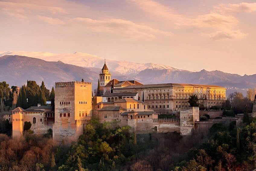 A historic building complex with a prominent tower, surrounded by mountains and trees. 1