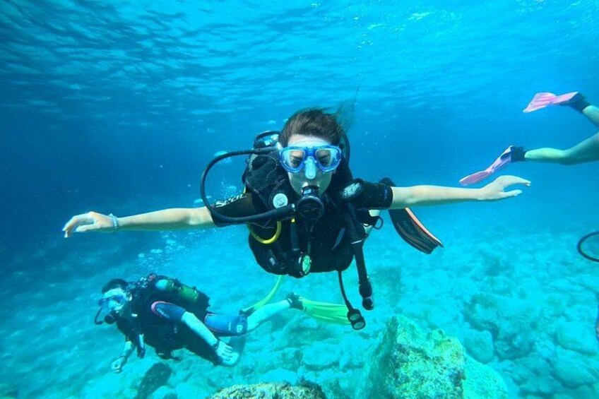 A diver with a scuba tank and fins, underwater with a clear blue ocean background. 1