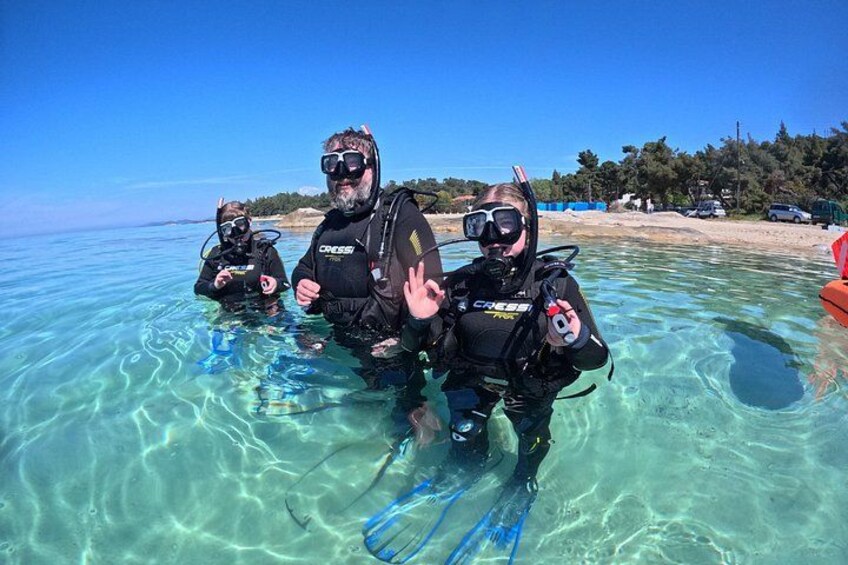 Three scuba divers in clear water with a beach and trees in the background. 4