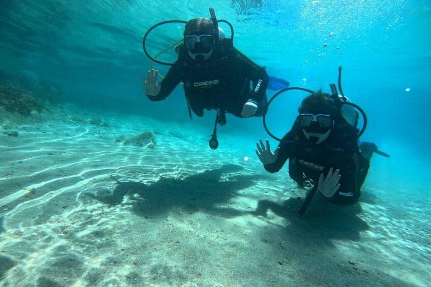 Two scuba divers underwater with fins and tanks, surrounded by sandy ocean floor and clear water. 5