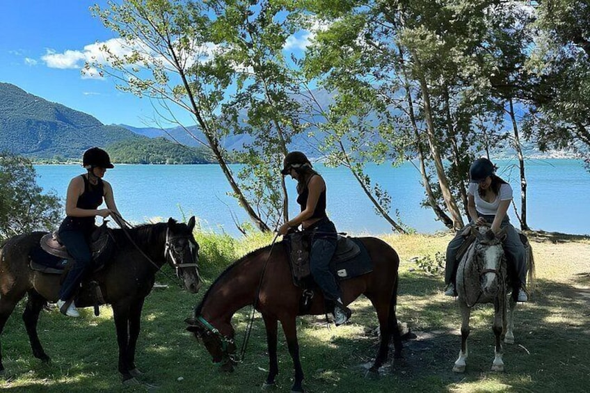 Trois personnes à cheval, au bord d’un lac, avec des arbres et des montagnes en arrière-plan. 2