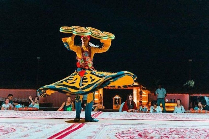 A performer balancing plates on their head, dressed in traditional attire, with an audience in the background. 5