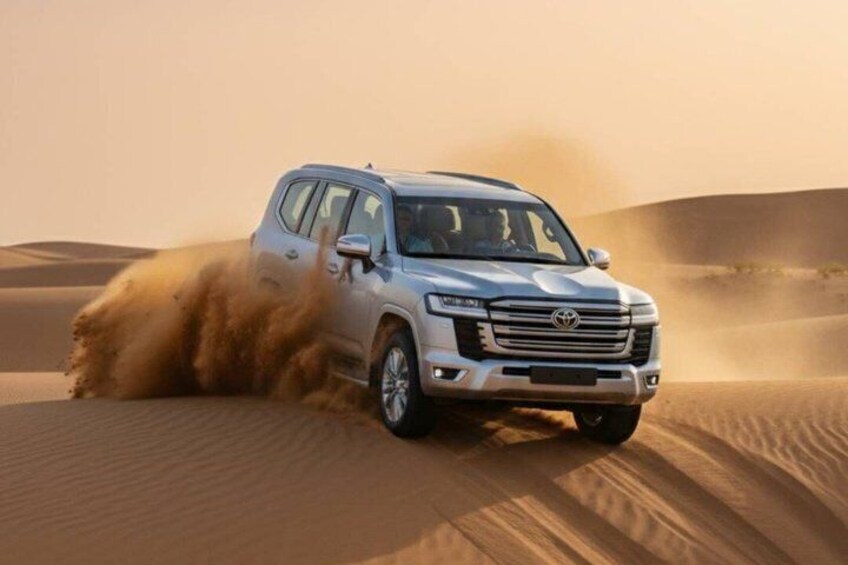 A silver SUV driving through a desert with sand dunes. 5