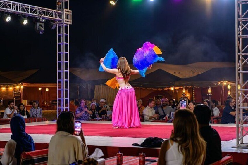 A person in a pink dress performing on a stage with a desert backdrop. 5