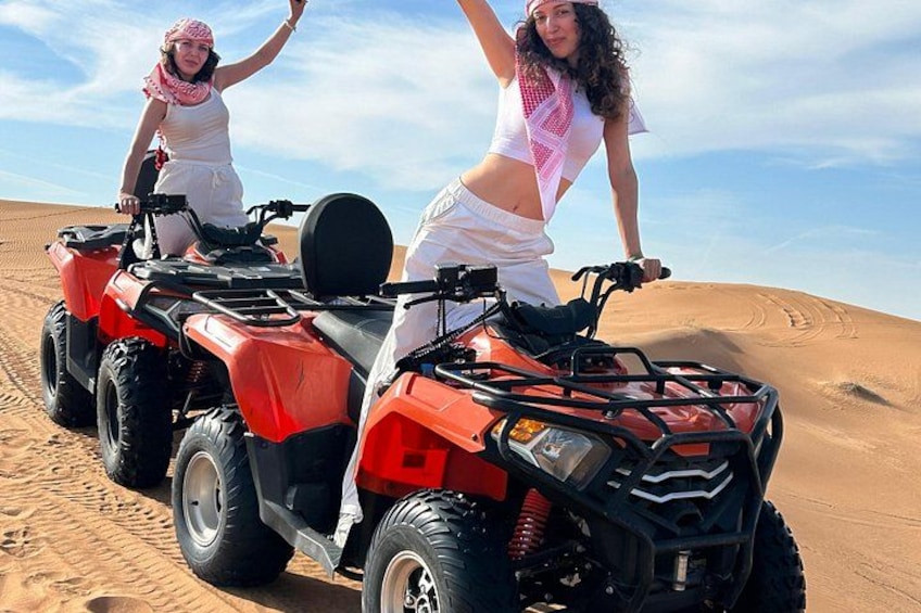 Two people on a red quad bike in a desert with sand dunes. 1